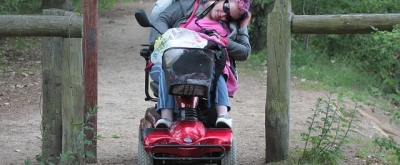 Rollstuhlfahrerin auf einem Waldweg bückt sich unter einem Hinderniss