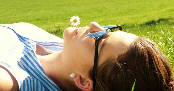 Frau liegt in der Sonne und hat eine Löwenzahnblüte im Mund