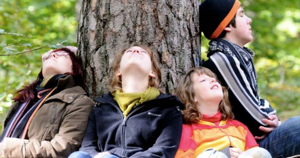 Eine Familie sitzt auf dem Waldboden und leht an einem Baumstamm