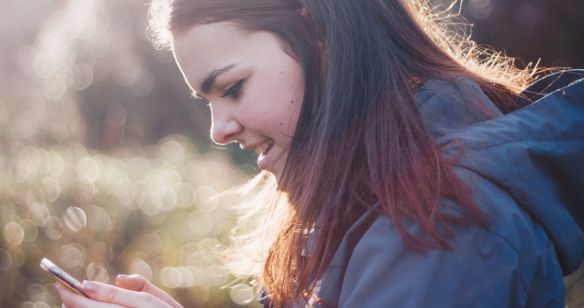 Junge Frau in der Natur schaut auf ihr Smartphone