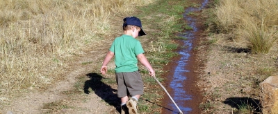 Kind wandert Feldweg - mit einem Stock in der Hand - entlang