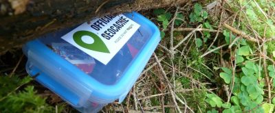 Ein Geocache ist im Wald unter einem Baum versteckt