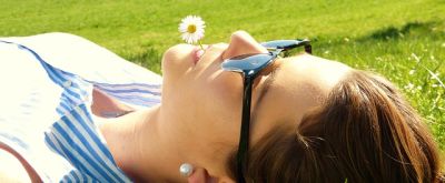 Frau in der Sonne Frau liegt in der Sonne und hat eine Löwenzahnblüte im Mund