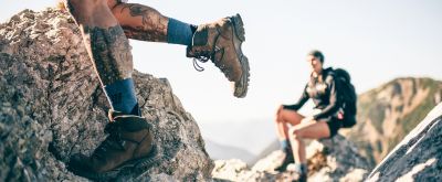 Wandersocken mit Kompression Beine eines Wanderers der Wandersocken in seinen Wanderschuhen trägt.