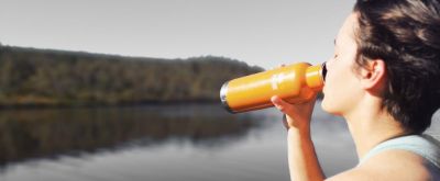 Trinken beim Wandern Mann steht in der Natur an einem See und trinkt Wasser aus einer Flasche