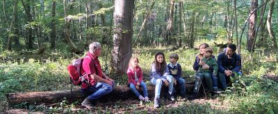 Wald-Entdecker-Tour Eine Familie sitzt auf einem Baumstamm im Wald