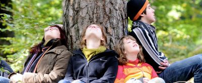 Eine Familie sitzt auf dem Waldboden und leht an einem Baumstamm