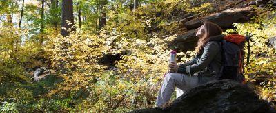 Wanderin sitzt im Wald auf einem Stein und genießt den Ausblick