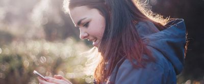 Junge Frau in der Natur schaut auf ihr Smartphone