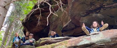 Wildnisschule: Eins mit der Natur Kinder sitzen im Wald auf einem Felsen