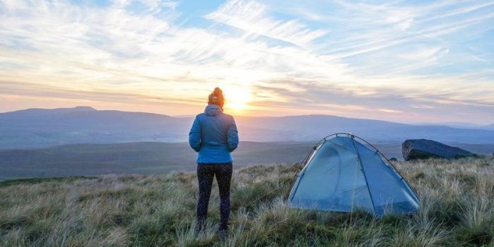 Kathrin Heckmann steht neben ihrem Zelt und betrachtet den Sonnenaufgang