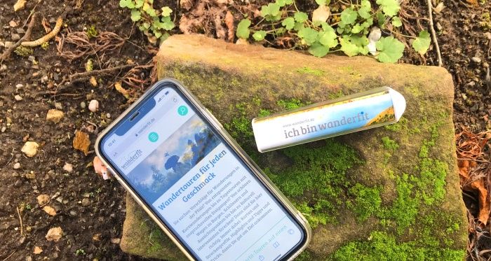 Die Wanderfit-App Smartphone mit Wanderphone App sowie Powerbank liegt in der Natur