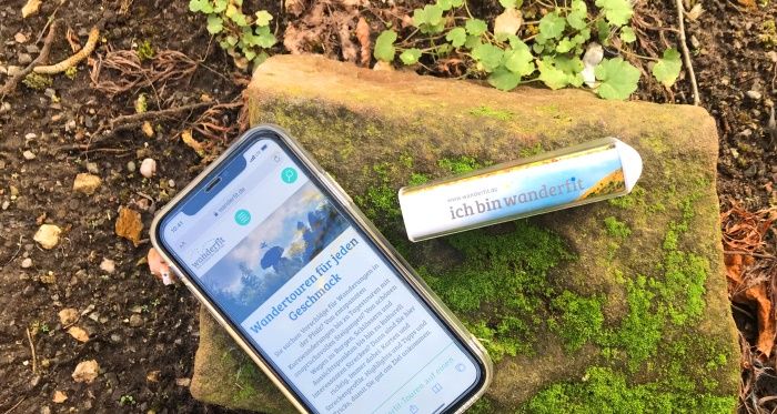 Smartphone mit Wanderphone App sowie Powerbank liegt in der Natur