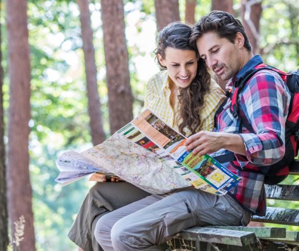 Zwei Wanderer sitzen auf einer Bank und schauen auf eine Wanderkarte